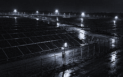Night camera view of solar panels behind a perimeter fence